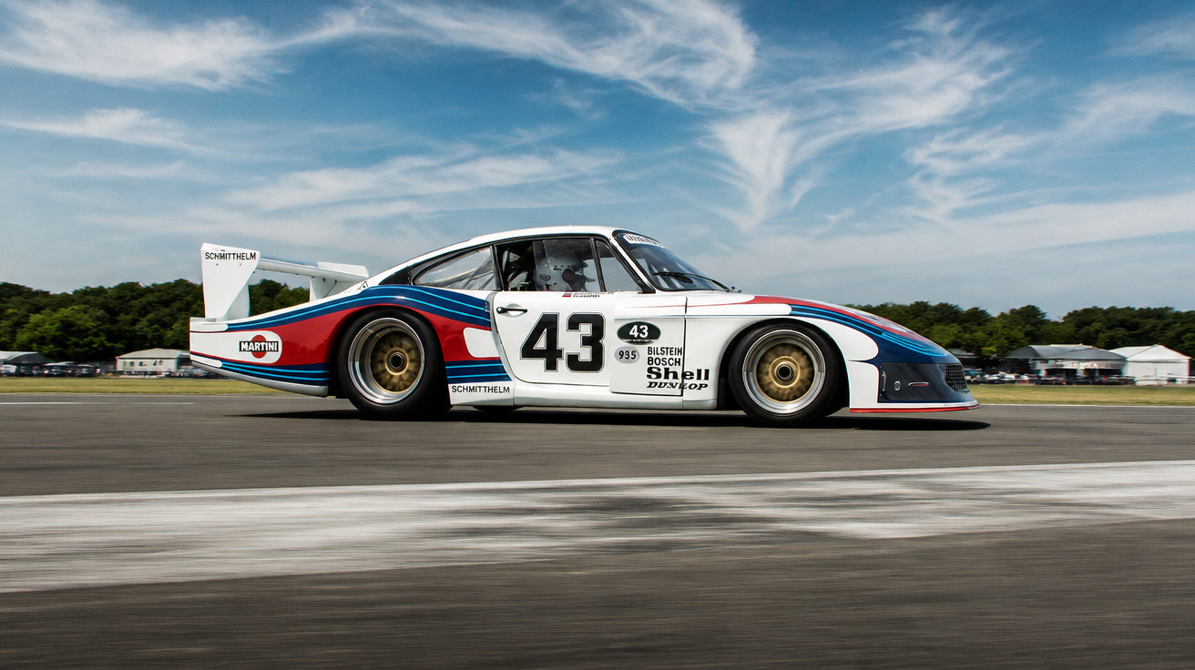 Weißer Porsche Rennwagen mit Nummer 43 und Martini-Racing-Lackierung auf Rennstrecke bei bewölktem Himmel.