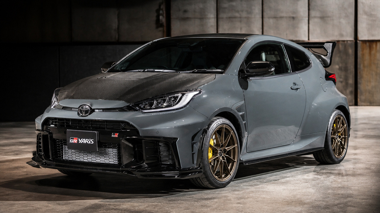 Grauer Toyota GR Yaris mit Carbon-Motorhaube und goldenen Felgen in dunkler Garage.