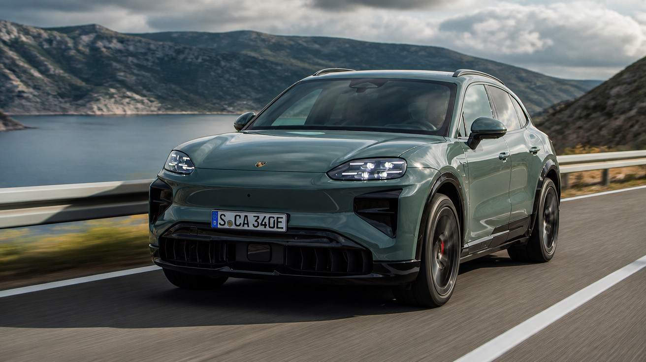 Grüner Porsche SUV fährt auf kurviger Straße am See mit Bergen und bewölktem Himmel im Hintergrund.